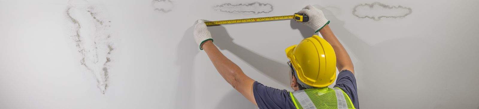 A male worker measuring water damage on a ceiling